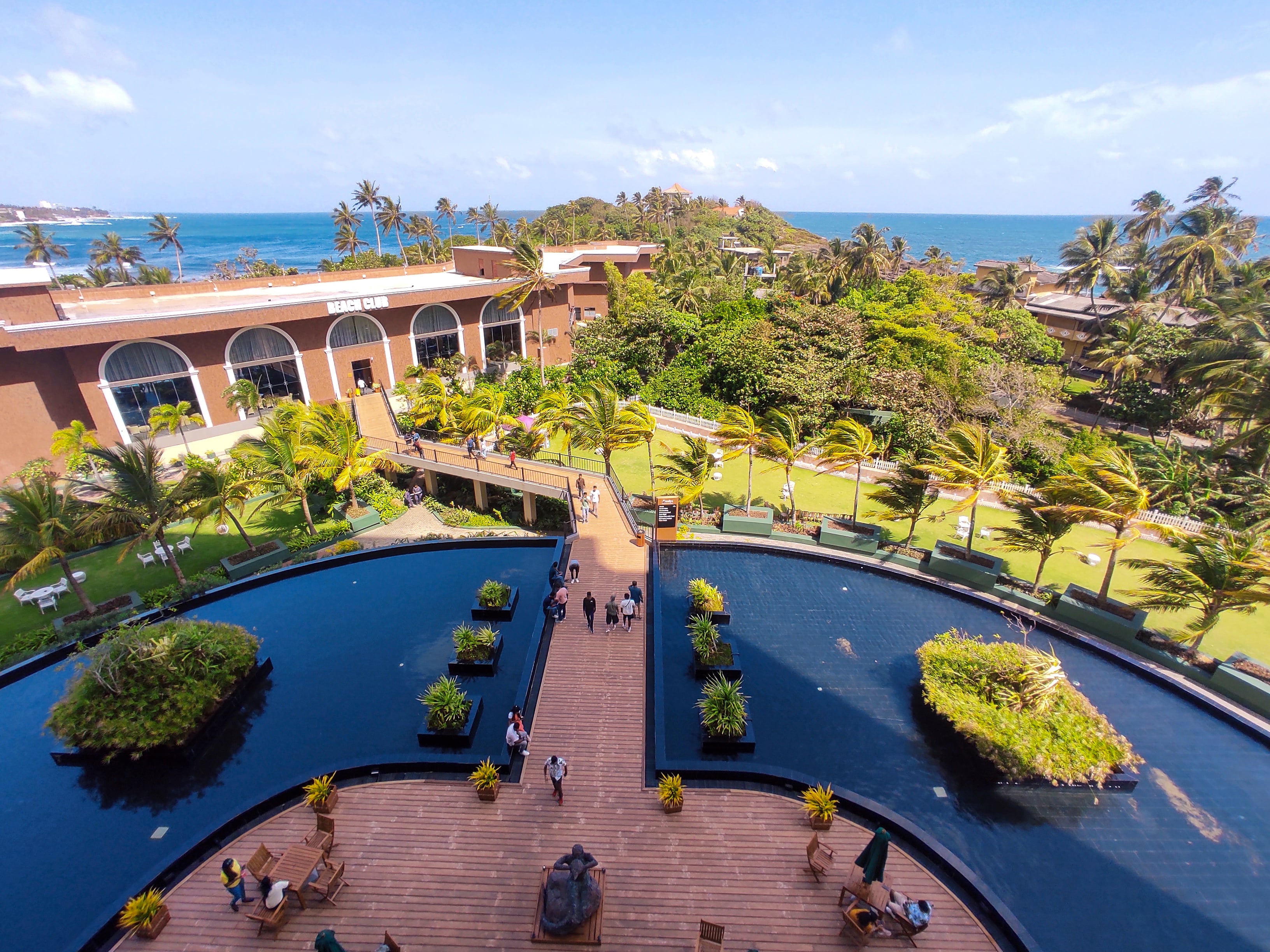 A stunning high-angle balcony view of the Araliya Hotel, showing its large water features, palm trees, and the blue ocean beyond.