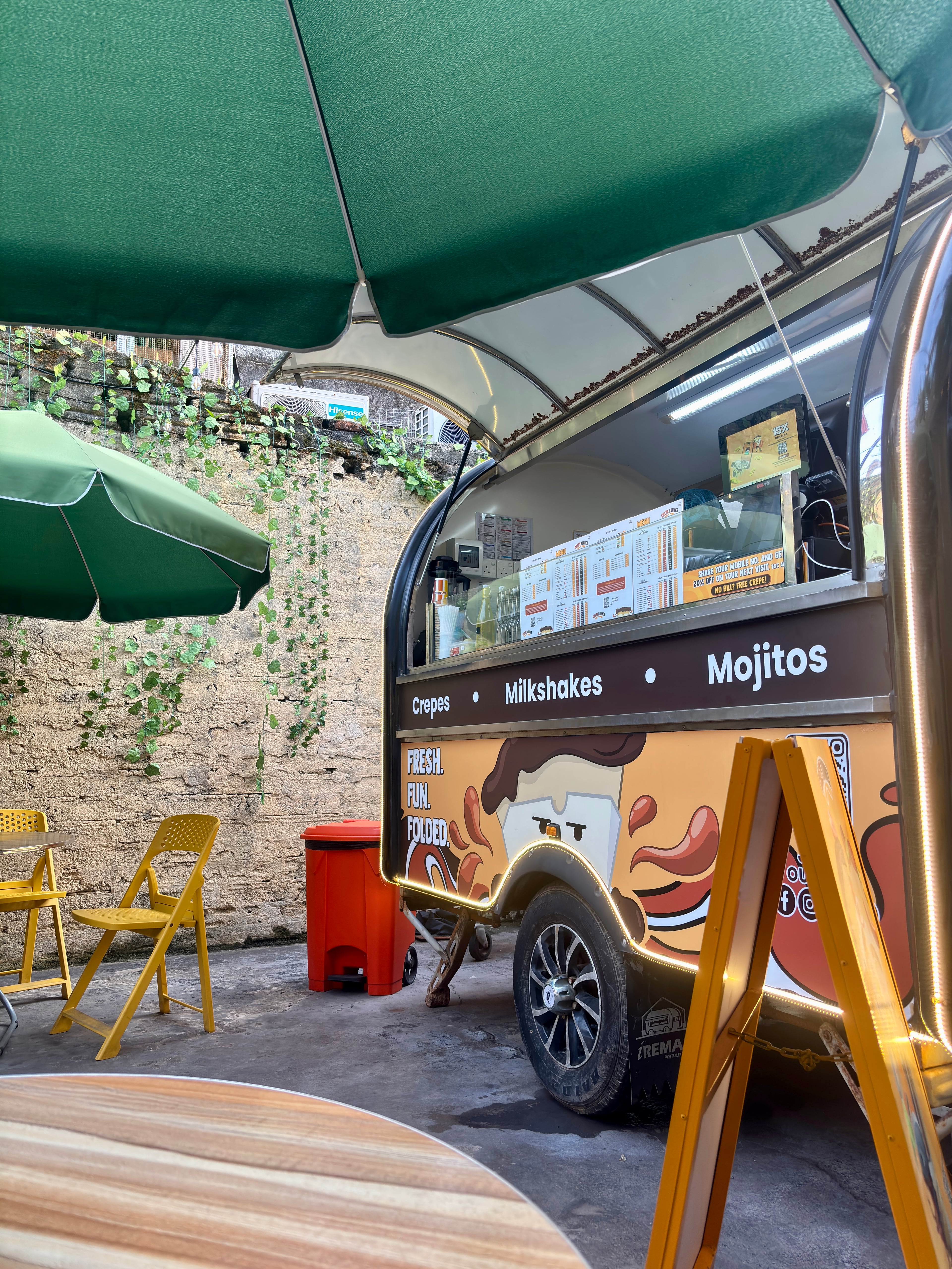 A vibrant food truck named Crepe Runners with green umbrellas and yellow chairs in an alleyway in Galle Fort