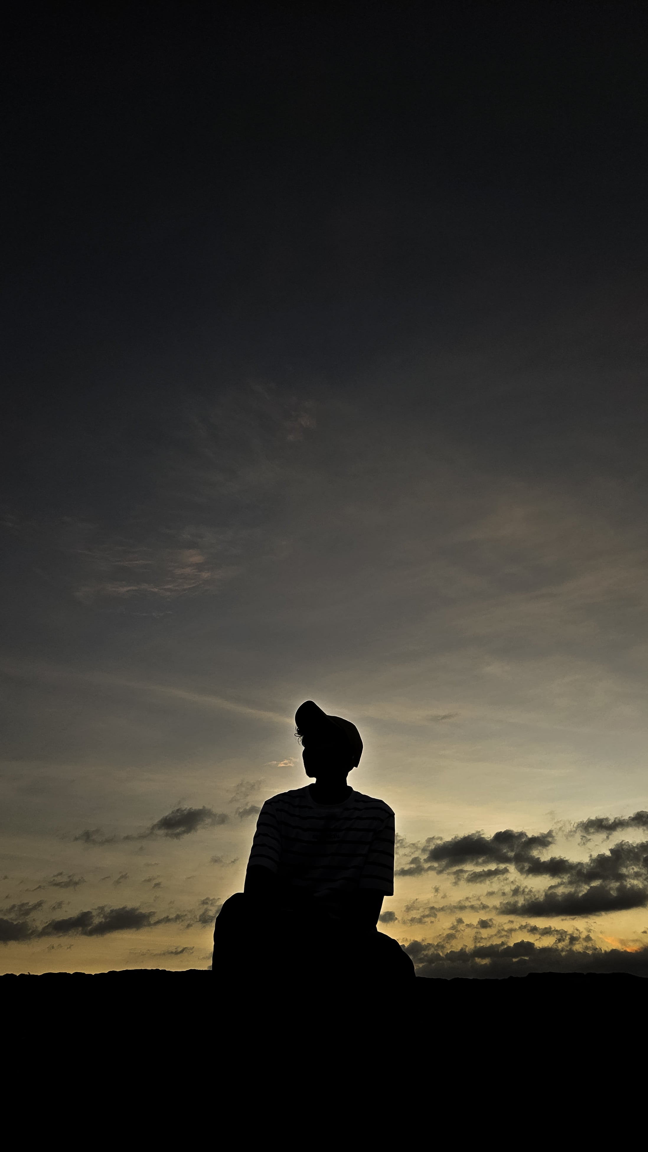 Silhouette of a person sitting alone against a moody, dusky sky with faint clouds