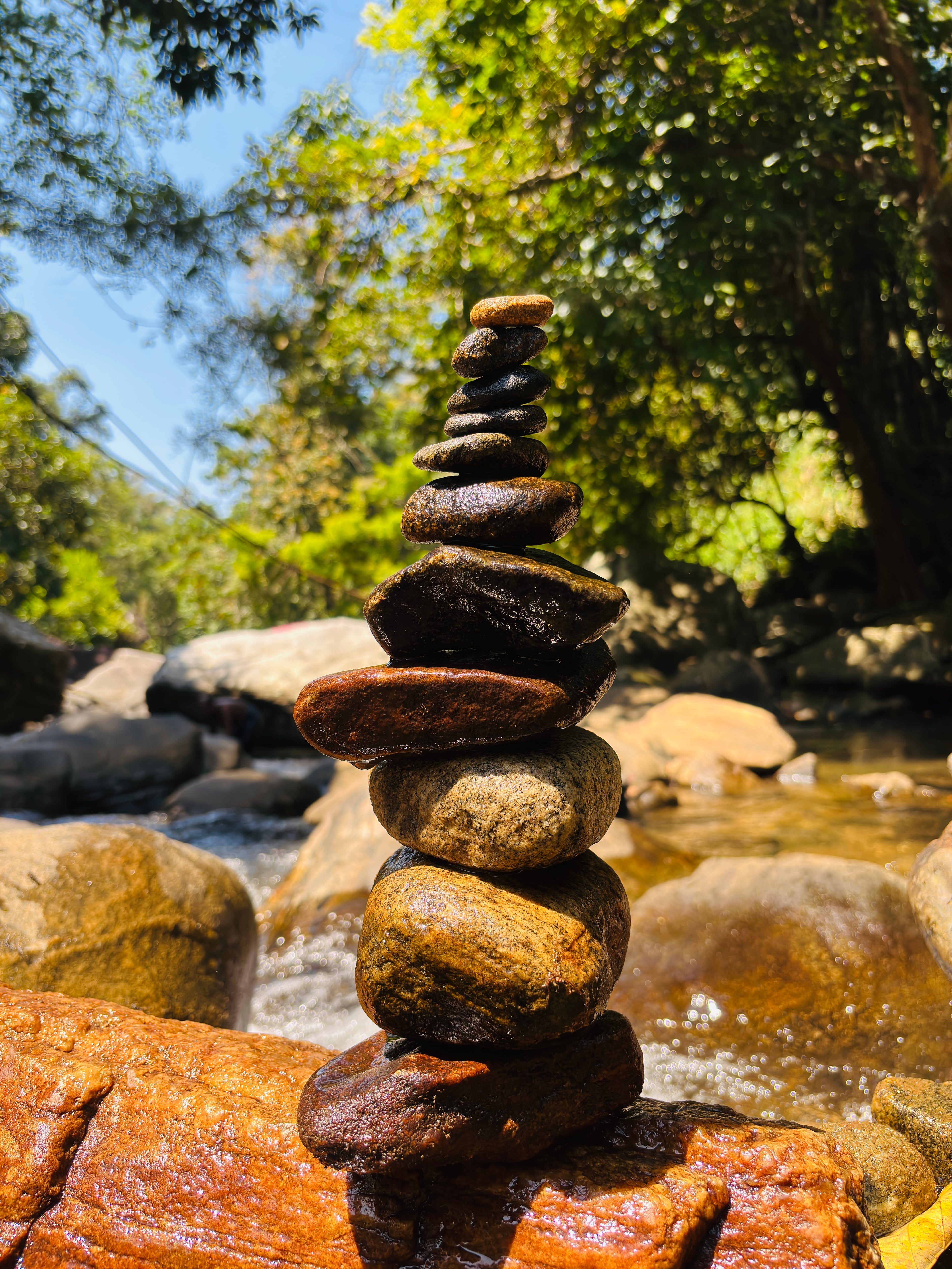A balanced stack of wet river stones with a blurred background of a stream and green trees