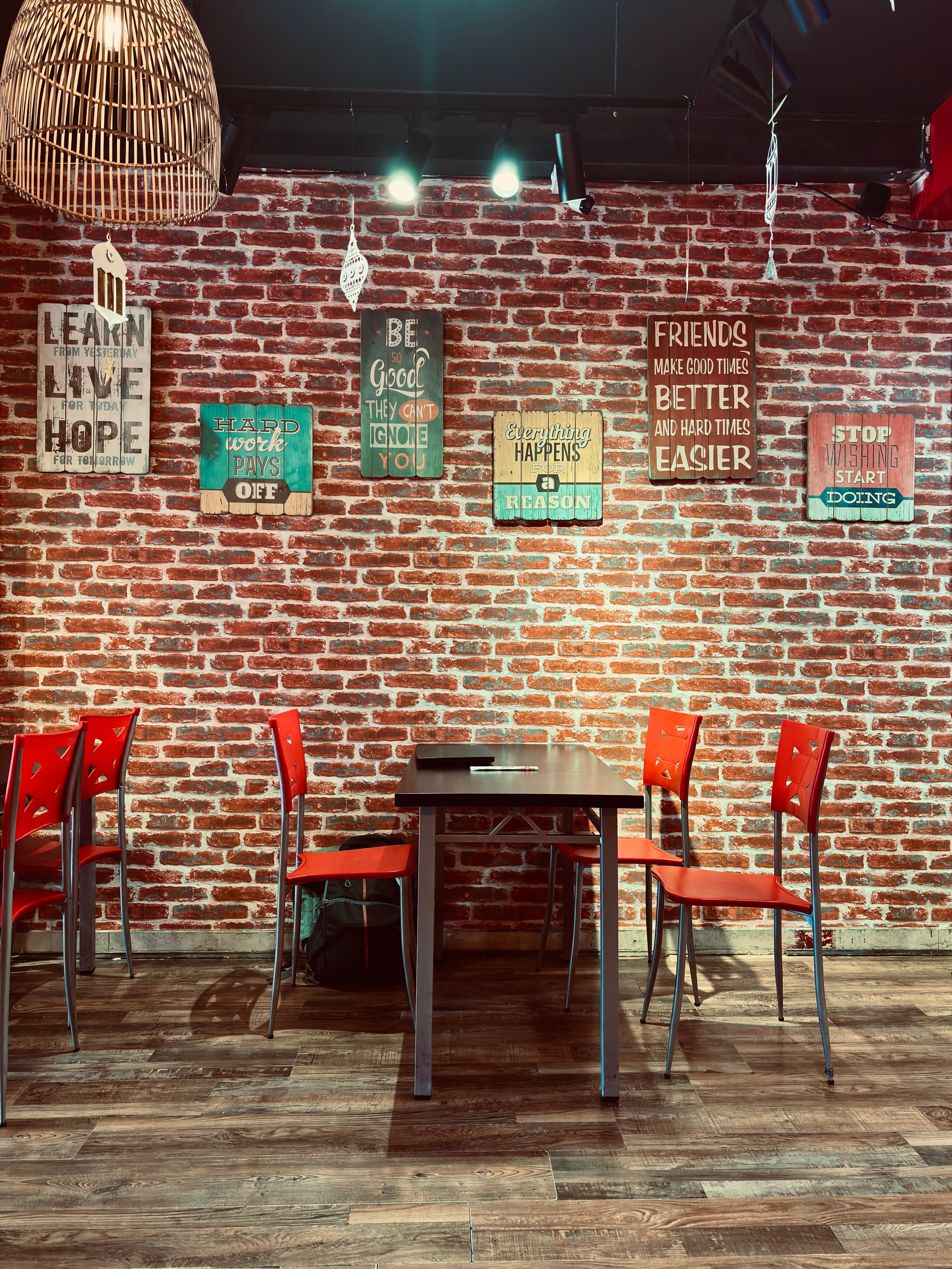 A cafe interior with red chairs, dark wooden tables, and a brick wall decorated with wooden motivational signs under warm lighting