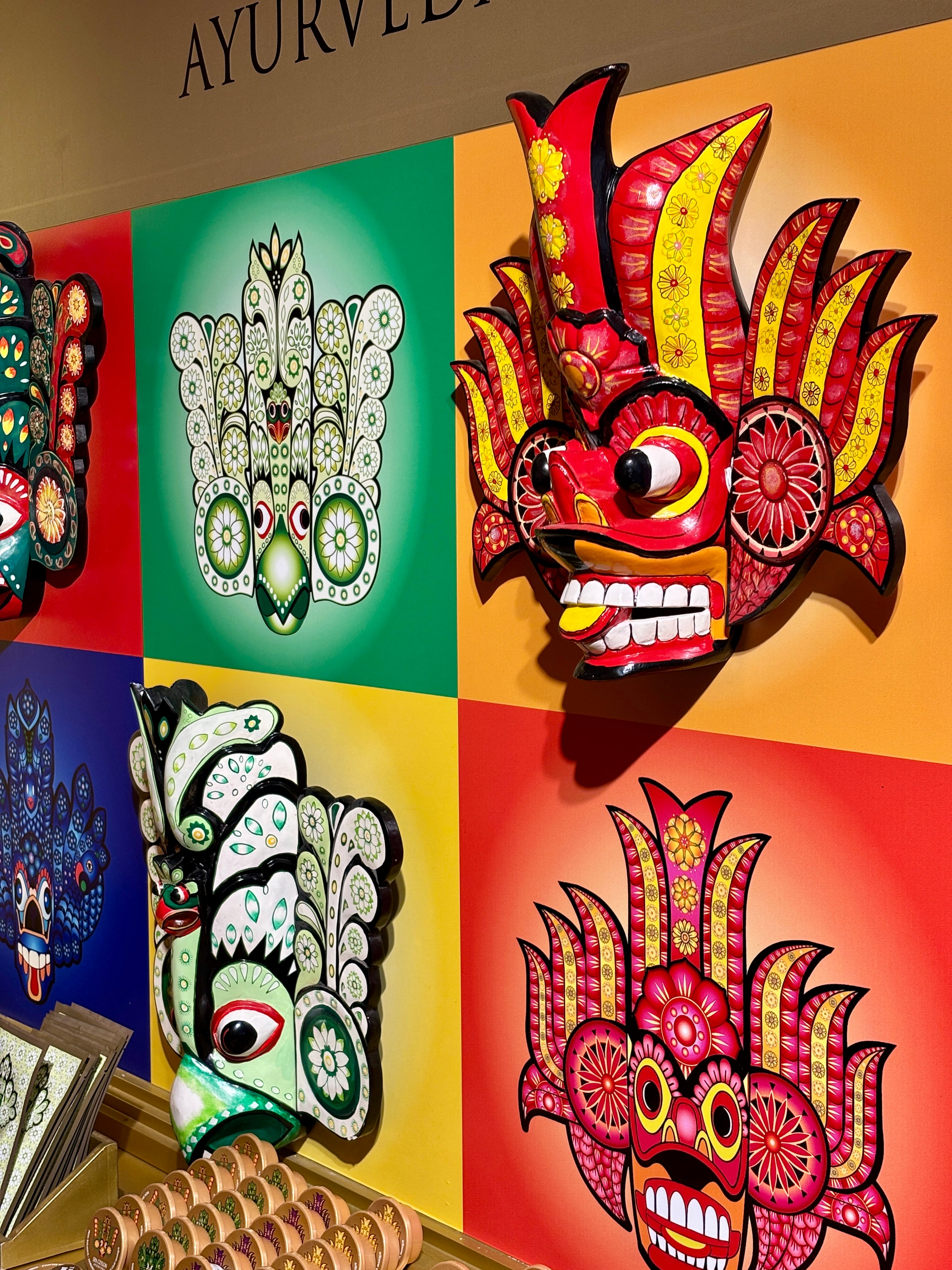 Colorful traditional Sri Lankan wooden Raksha masks displayed on a brightly painted wall