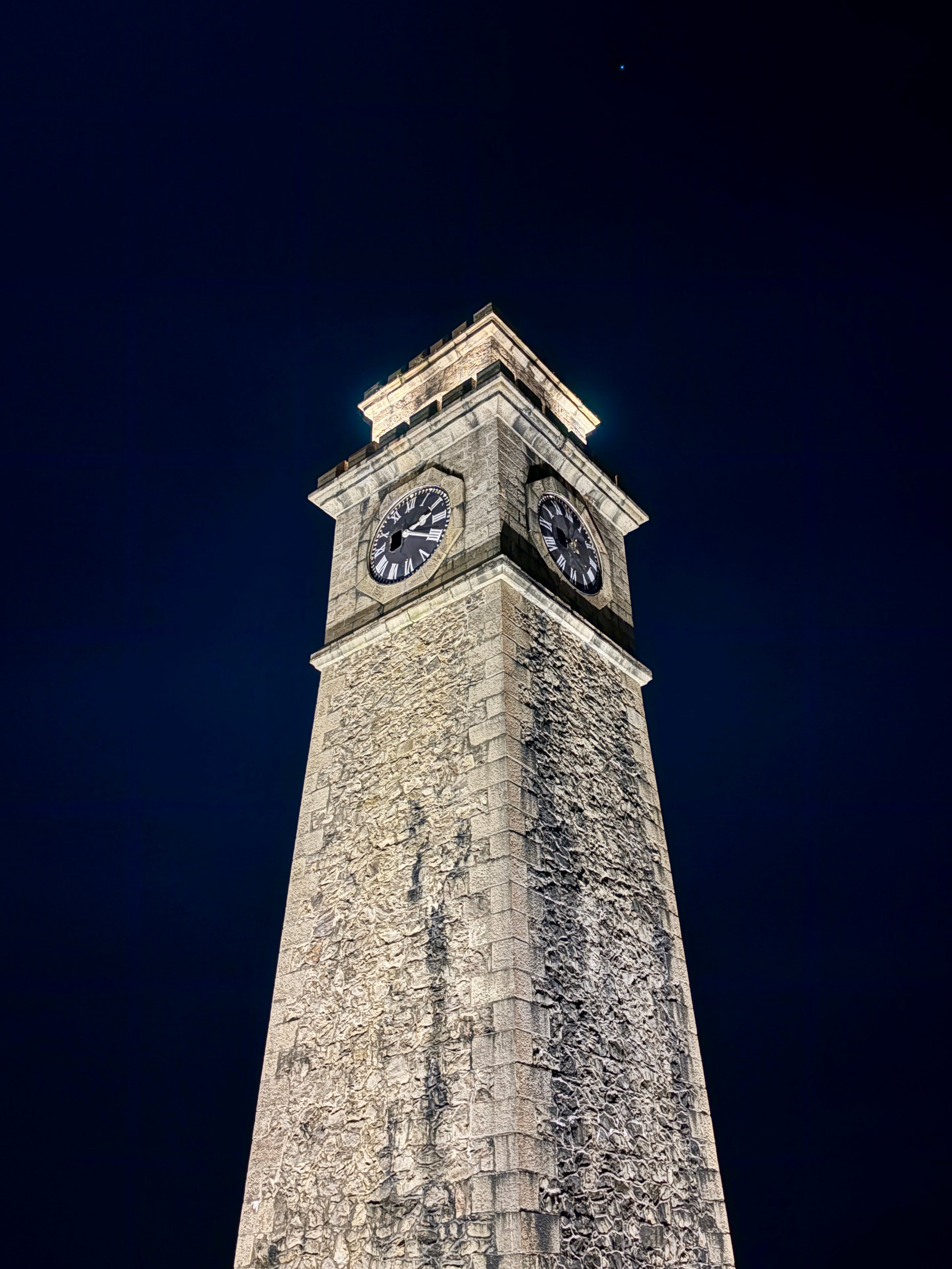 A historic stone clock tower illuminated against a dark blue night sky