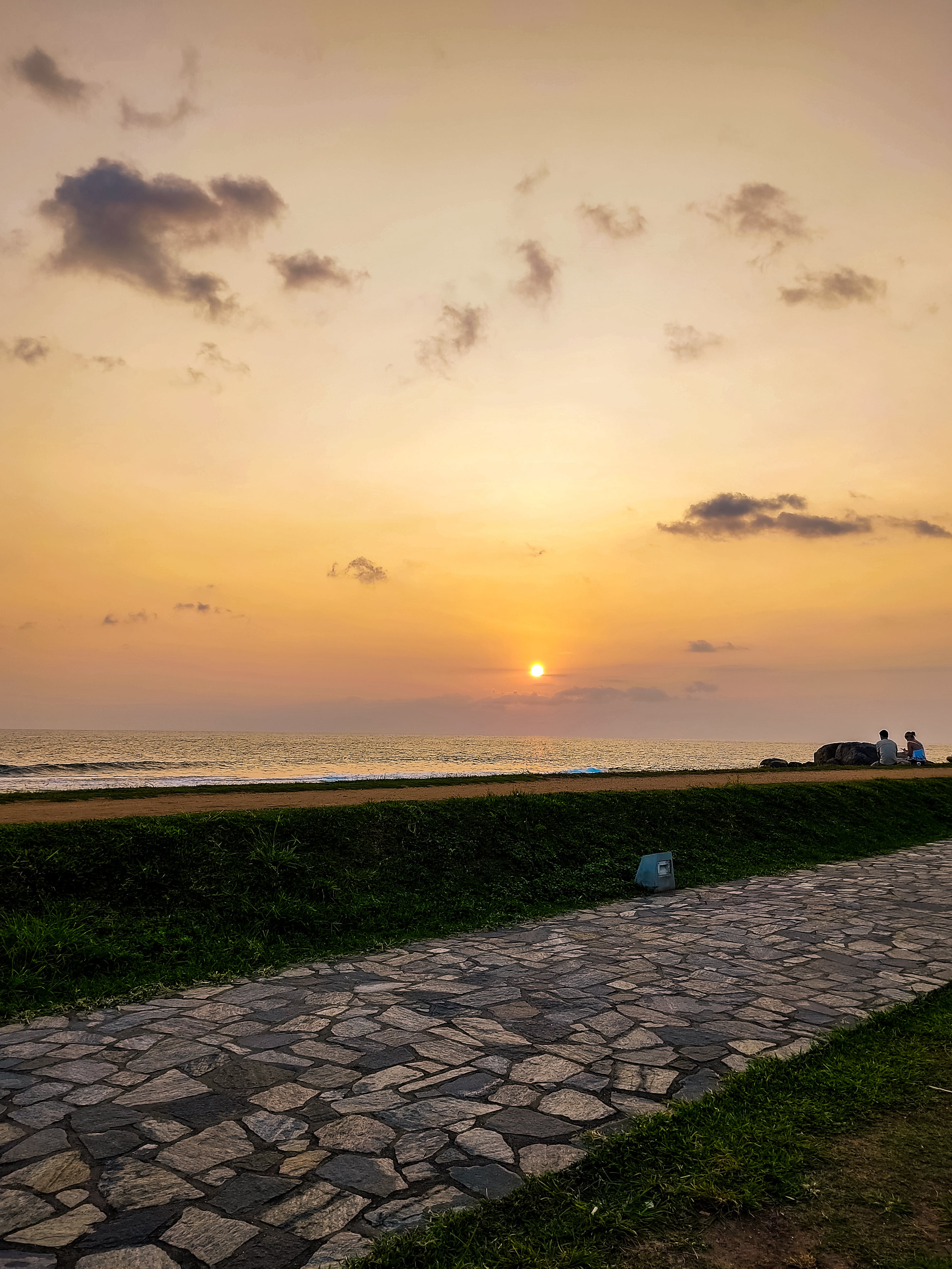 A warm, golden sunset over the ocean horizon with a stone walkway in Galle Fort in the foreground