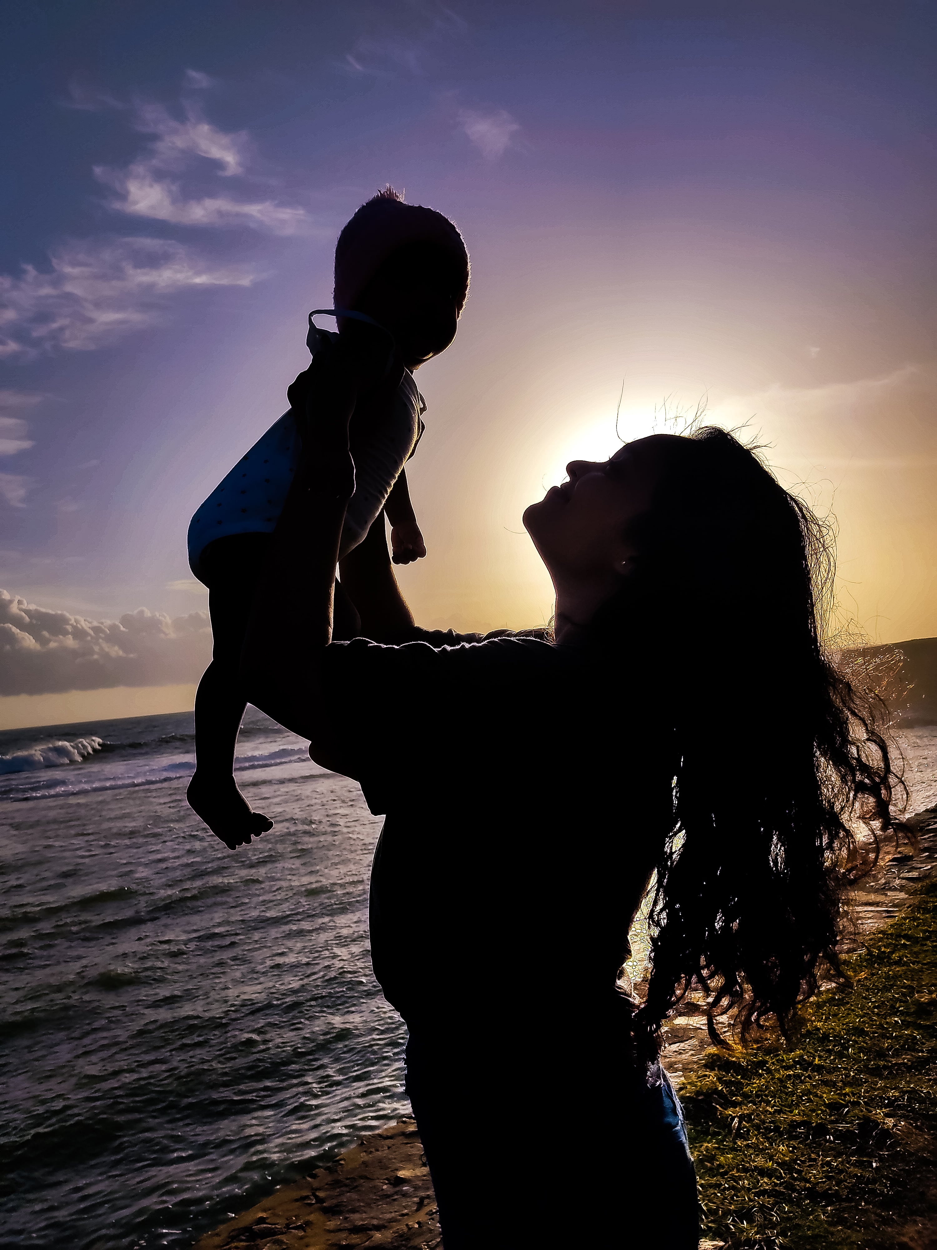 Silhouette of a mother lifting her child into the air against a vibrant sunset over the sea