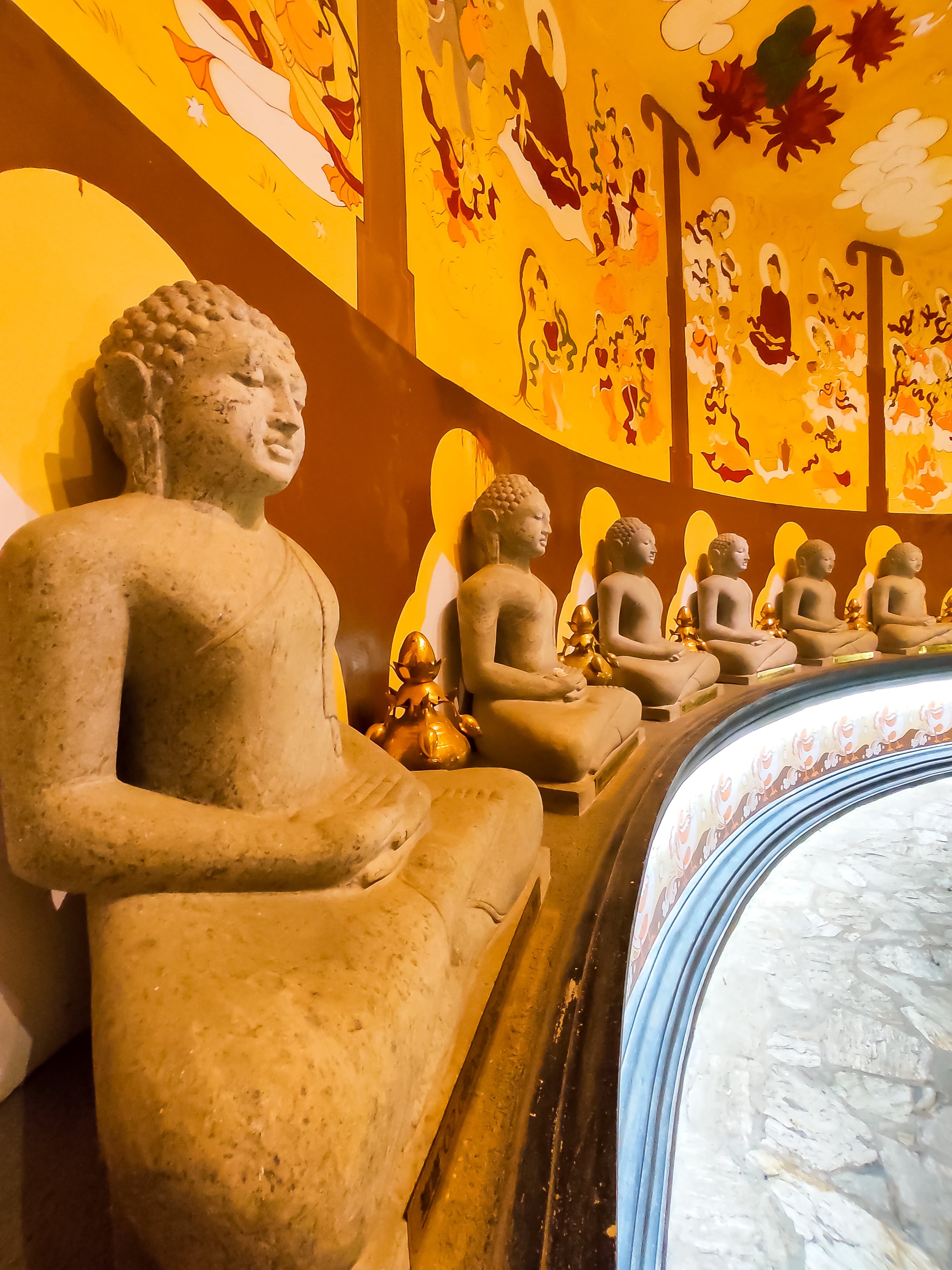 A row of stone Buddha statues arranged along a curved wall inside a temple with warm, golden lighting